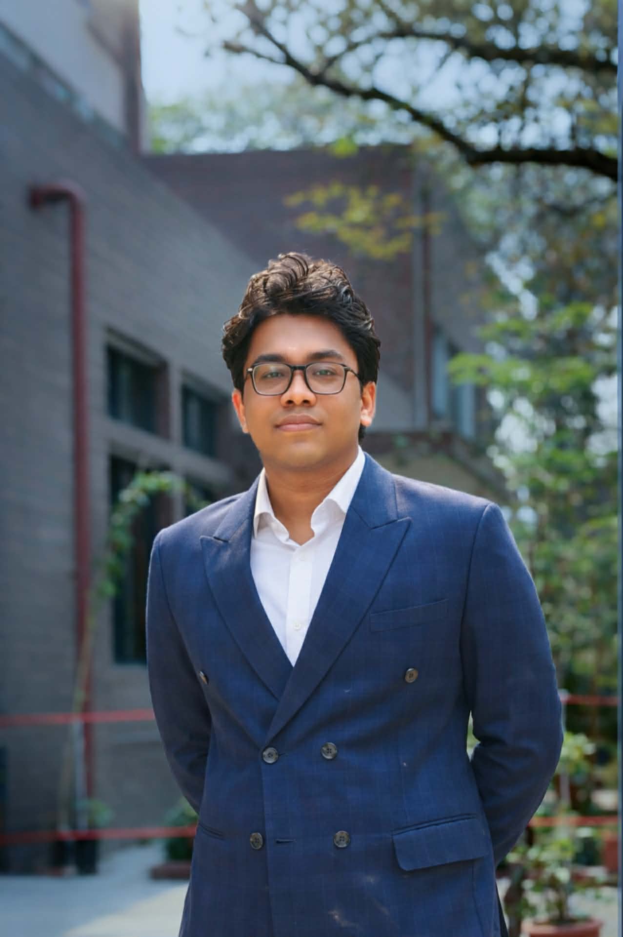 Mostafa Tahmeed Foysal, wearing a navy suit and glasses, outdoors